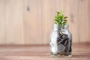 un bocal rempli de pieces de monnaie avec une petite plante verte dessus